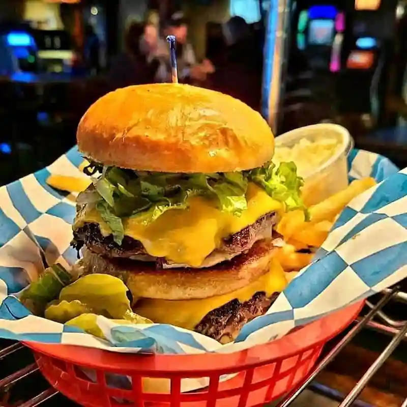 A stacked cheeseburger in a checkered basket with the arcade glowing behind