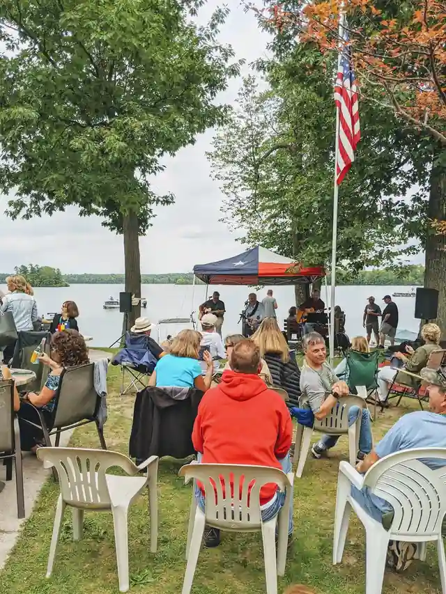 A crowd sitting on the lawn at an outdoor event by the lake, seen from behind