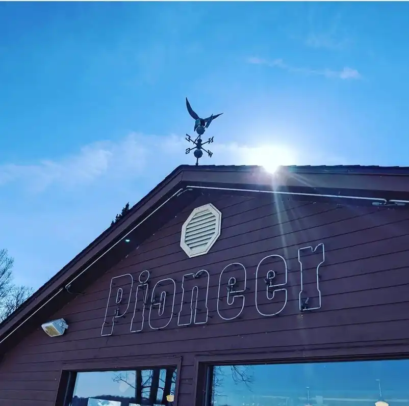 Pioneer lettering on the gable of the bar building under an eagle weathervane and blue sky